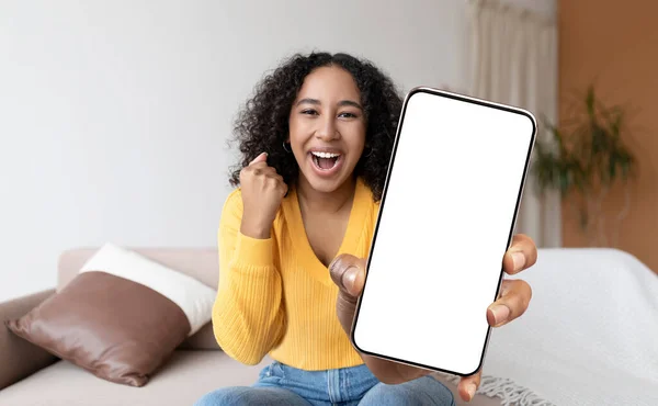 Excited Black Young Woman Sitting On Couch And Showing Big Blank Smartphone At Camera, Happy African American Female Holding Device With White Screen And Celebrating Success, Collage, Mockup