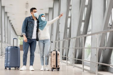 Tıbbi Yüz Maskeli Genç Müslüman Eşler, Havalimanında Bavulları Terminalde Bekleyen Mutlu Orta Doğu Çifti, Uzaktaki Uçağı Gösteren Kadın, Kopya Alanı
