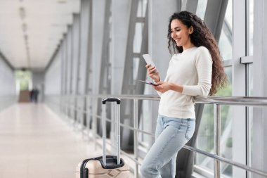 Havaalanında beklerken Smartphone kullanan güzel genç bir kadının portresi, Terminalde bavulla dururken gülümseyen Orta Doğulu bir bayanın cep telefonuna bakması, Boşluğu Kopyala
