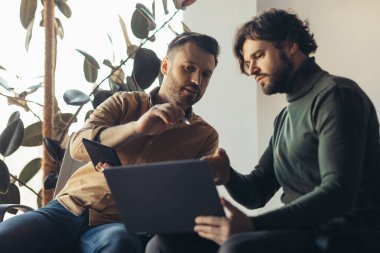 Modern ofisteki dizüstü bilgisayar ve tablet bilgisayarları kullanarak iş projesinde birlikte çalışan erkek meslektaşlarıma odaklandım. Şirket toplantısı, beyin fırtınası, takım çalışması ve işbirliği konsepti
