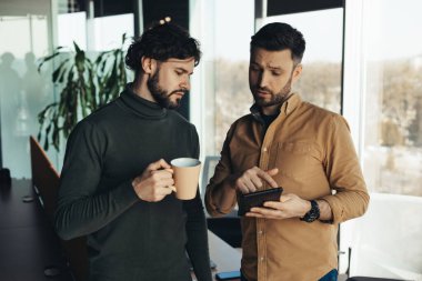 Dijital tablet kullanan, iş projesini tartışan, modern ofiste kahve içen iki ciddi iş arkadaşının portresi. Takım çalışması, işbirliği ve birlikte çalışma kavramı