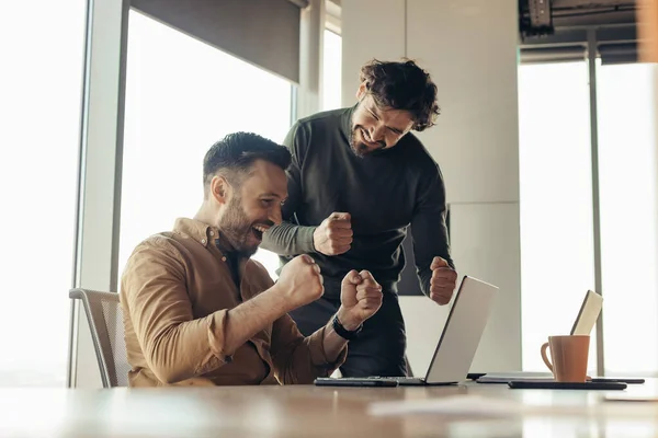 Achieving success, professional triumph concept. Excited male coworkers celebrating achievement, making great deal or agreement, gesturing YES near laptop at modern office