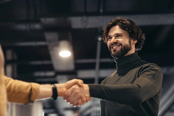 Business partnership concept. Smiling entrepreneur handshaking with partner after successful negotiations at modern office. Happy male businessman greeting companion after signing contract