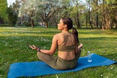 Nilüfer çiçeği pozunda meditasyon yapan, sabah yoga yapan, Gyan Mudra yapan, zen 'e uzanan, açık havada spor minderinde oturan genç siyahi bir kadın. Boşluğu kopyala