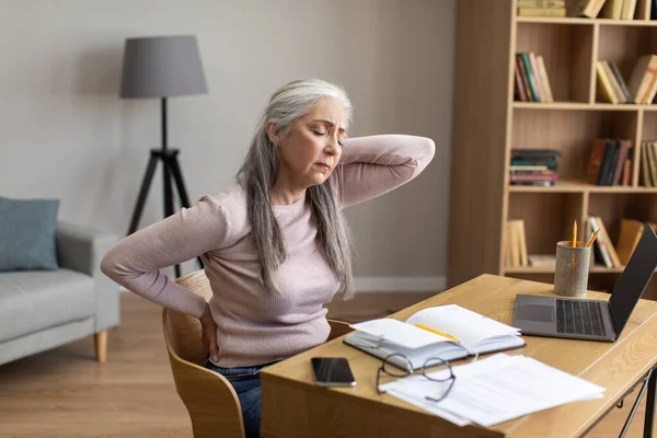 悲伤疲惫的欧洲老人灰白头发的女性做背部按摩 与笔记本电脑在客厅内部 自由自在的空间 家庭教育和学习 健康问题 因Covid 19大流行病造成的过度工作 — 图库照片