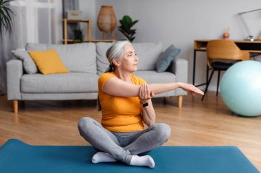 Aktif kıdemli kadın evde kolunu paspasın üzerine uzatıyor, esneklik egzersizleri yapıyor, yoga yapıyor ya da evde pilates yapıyor. Emeklilik kavramı üzerine iç eğitim