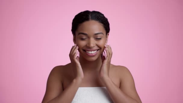 自然の美しさのケア スタジオポートレートの幸せな美しいアフリカ系アメリカ人女性ラップでタオルで彼女の顔に触れ 笑顔でカメラにピンクの背景 スローモーション — ストック動画
