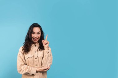 Neşeli bin yıllık Kafkas bayan esmer kız öğrenci gündelik gösteriş yapıyor, bir fikri var, mavi arka planda, stüdyoda izole edilmiş. El işareti, insani duygu, yüz ifadesi, harika reklam, satış ve teklif.