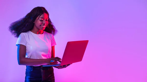 ラップトップPcを使用して陽気な若い黒人女性の肖像画 勉強やリモートで作業 ネオンライトでオンライン会議を持っています 空のスペースとバナー アフリカ系アメリカ人女性のウェブ閲覧 — ストック写真