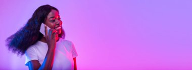 Gülümseyen genç Afrikalı Amerikalı kadın cep telefonuyla neon ışıkta konuşuyor, afiş tasarımı ve fotokopi alanı. Güzel siyahi bayan müşteriyle ya da arkadaşıyla akıllı telefondan konuşuyor.