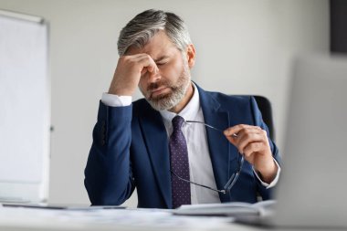 İşyerinde baş ağrısı çeken orta yaşlı işadamı, akut migren ya da göz rahatsızlığı olan yorgun bir girişimci, modern ofiste çalışırken kendini iyi hissetmiyor.