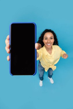 Mavi stüdyo arka planında boş ekranı olan akıllı telefonu gösteren güzel bir bayan. Milenyum kadını yeni mobil uygulama, reklam sitesi, fotokopi alanı öneriyor. Görünümün üstünde