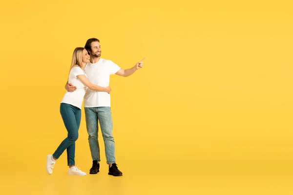 白いTシャツの幸せな千年紀の白人男性と女性の抱擁と空の空間で指を指して 黄色の背景に隔離され 完全な長さ スタジオ ロマンス オファー — ストック写真