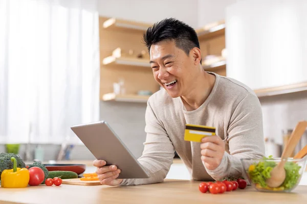 快乐的中年男子上网购买食物 使用全新的数码平板电脑和塑料信用卡 购买健康晚餐的配料 在家为家人做饭 复制空间 — 图库照片
