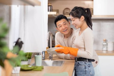 Sevgili koca yakışıklı, orta yaşlı Asyalı adam karısını desteklerken güzel genç bayan bulaşıkları yıkıyor, sohbet ediyor ve gülümsüyor lastik eldiven takan kadın, fotokopi odası.