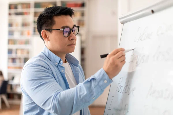 Middle Aged Korean Teacher Man Writing Grammar Rules On Whiteboard Having Class Standing In Modern Classroom Indoor. Knowledge And School Education Concept. Selective Focus