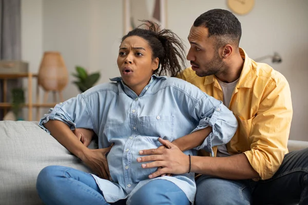 怀孕的黑人女士在家里和丈夫一起坐在沙发上分娩疼痛 男人在生孩子的时候支持女人 家庭生活方式 怀孕和分娩概念 — 图库照片