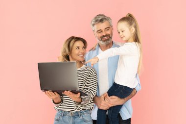 Pembe Stüdyo Arkaplanı Üzerinde Bilgisayar Reklamcılığı Web sitesini işaret eden Çocuk Kız ve Ebeveynler Birlikte Dizüstü bilgisayar kullanıyor. İnternette gezinen üç kişilik bir aile. Kaynaklar ve Teknoloji