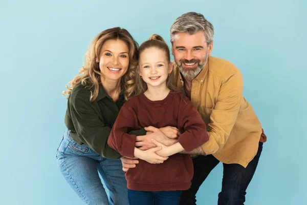 Family. Middle Aged Father And Mother Embracing Little Daughter Posing Together Smiling To Camera Over Blue Background In Studio. Shot Of Happy Parents And Kid