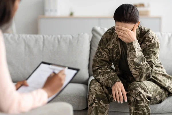 Psychotherapy With Veterans. Depressed Female Soldier Having Counselling Meeting With Psychiatrist In Office, Upset Military Female In Uniform Sitting On Couch And Crying, Covering Face In Despair