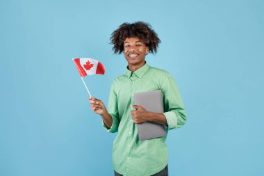Modern eğitim ve öğrenci değişimi. Kanada 'nın küçük bayrağını elinde tutan mutlu siyah adam ve kameraya gülümsüyor, mavi arka planda duruyor, stüdyo çekimi, kopyalama alanı