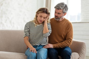 Baş ağrısı. Eşine destek olan koca, evde koltukta oturan ağrılı migren dokunuşundan muzdarip. Hipertansiyon Semptomu, Kadın Sağlık Sorunları Konsepti