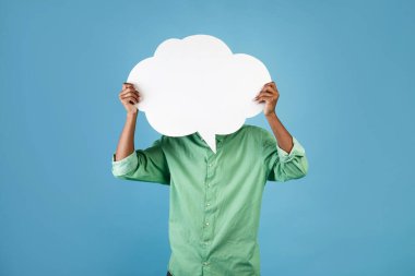 Tanımlanamayan Afrikalı Amerikalı genç adam kafasının önünde boş bir konuşma balonu tutuyor, mavi stüdyo arka planında poz veriyor, bedava fotokopi alanı.