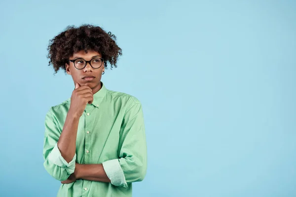 Pensive african american guy thinking over something on blue studio background, looking aside at free space. Puzzled black teenager deep on thought, making decision