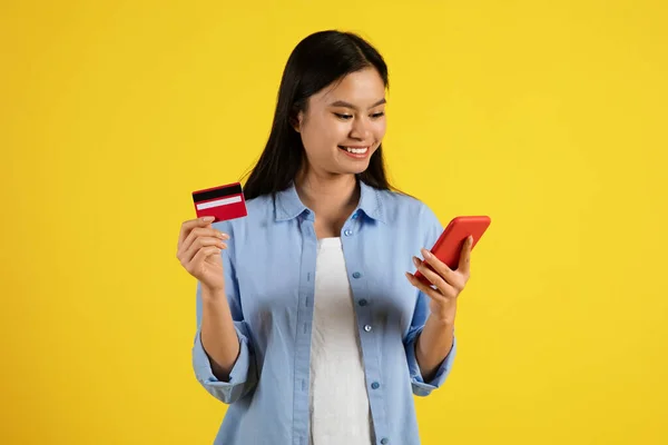 Uśmiechnięta Młoda Azjatka Patrzy Smartfona Pokazuje Kartę Kredytową Robi Zakupy — Zdjęcie stockowe