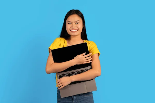 仕事や勉強のための近代的な技術 黄色のTシャツのダウン症候群を持つ幸せな若いアジアの女性は 青い背景 スタジオに隔離された空白の画面でノートパソコンを抱擁 良いオファー ウェブサイトや広告 — ストック写真