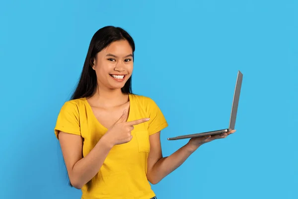 ウェブサイトの推薦 広告および提供 黄色のTシャツを着た若い中国人女性の笑顔ノートパソコンで指を指して 青の背景 スタジオに孤立した オンラインショッピング 仕事とブログのための近代的な技術 — ストック写真