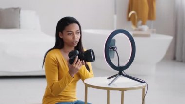 Profesyonel siyahi kadın fotoğrafçı, yeni fotoğraf makinesiyle ilgili video eleştirisi kaydediyor, akıllı telefondan abonelerle konuşuyor, yavaş çekimde.