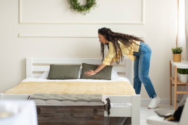 Neşeli genç bayan evde yatak yapıyor, yastık düzenliyor, sabahları ev işi yapıyor, fotokopi çekiyor. Pozitif milenyum kadını yatak odasını temizliyor. Günlük rutin konsept