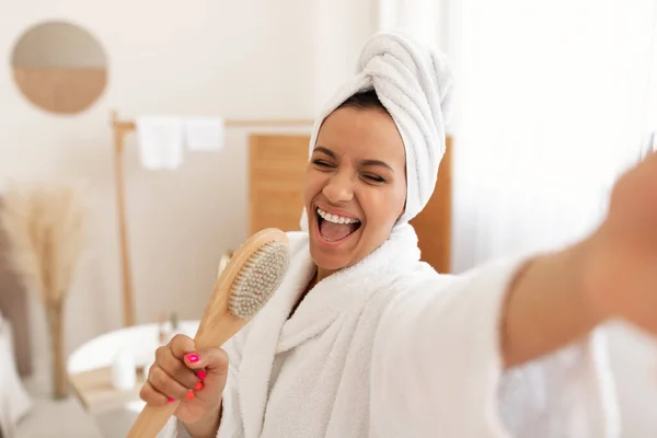 Joyful Black Lady Singing Holding Wooden Brush Having Fun Caring For Body Standing In Modern Bathroom At Home. Bodycare And Beauty Routine Concept. Selective Focus
