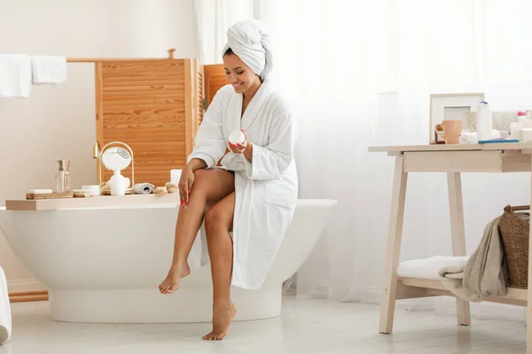 身体护理的概念 现代浴室室内 穿着白色浴衣坐着后 有魅力的女性保湿腿应用保湿霜 健康与美感概念 — 图库照片