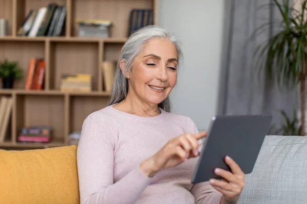 笑容满面的欧洲老年女性白发苍苍 在房间内的平板电脑上进行远程会面 聊天和观看视频 由于Covid 19的流行 商业课程 新的和新的应用程序在家里 — 图库照片
