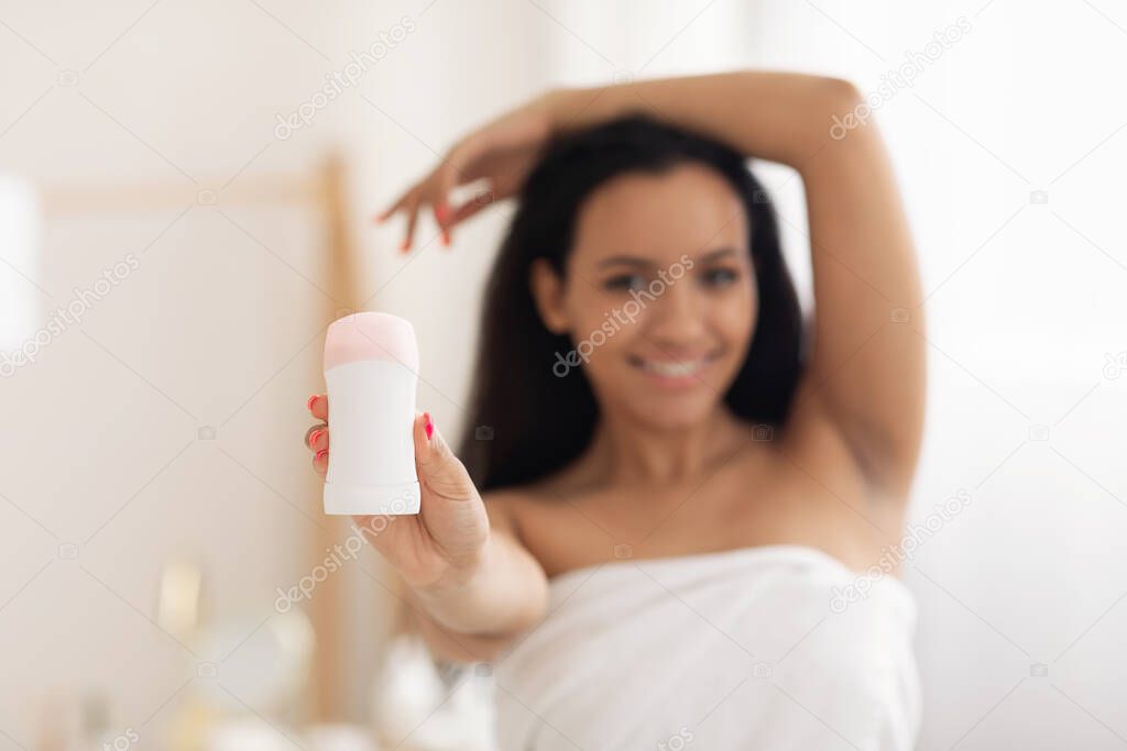 Happy Lady Showing Antiperspirant To Camera Advertising Product For Sweat Protection And Armpits Care Standing Wrapped In Towel In Modern Bathroom At Home. Bodycare Cosmetics. Selective Focus