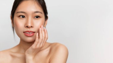 Şehvetli Koreli kadının portresi yumuşak tenine dokunuyor ve gülümsüyor, cilt bakımını seviyor, beyaz stüdyo arka planında poz veriyor, boş alanı olan bir panorama.