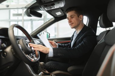 Mutlu sigorta acentası yeni arabasında oturuyor, otomobil bayii merkezinde otopark kontrolü yapıyor, boş bir alanda. Galeride satılmadan önce Milenyum Müdürü test sürüşü aracı