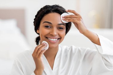 Günlük Skincare. Çekici siyahi bayan pamuklu pedlerle deriyi temizliyor, güzel Afro-Amerikan kadın makyajdan yüzünü temizliyor ve kameraya bakıyor, boş alanla yakın çekim yapıyor.