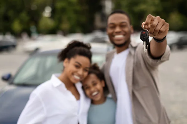 Car Purchase. Cheerful African American Family Holding Auto Key To Camera Standing Outside Near New Vehicle. Automobile Owners Concept. Selective Focus On Keys