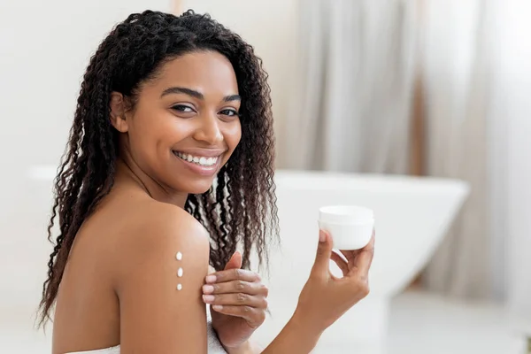 自我照顾的概念 年轻黑人妇女在皮肤上涂润肤润肤乳 快乐的非洲裔美国女性在浴室内涂了三道护肤乳霜 复印空间 — 图库照片