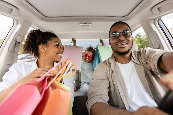 快乐的黑人家庭坐在车上拿着购物袋 快乐的购物狂父母和女儿在商场过了成功的周末后开车 商业和消费主义 — 图库照片
