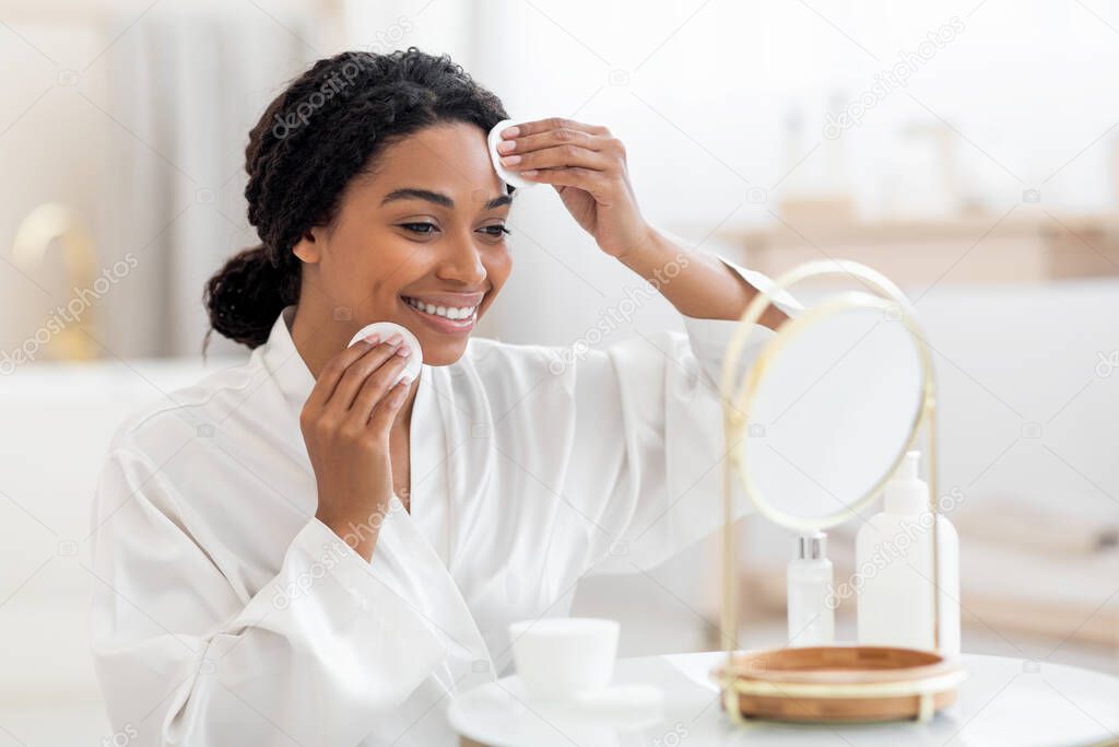 Beauty Routine. Smiling Black Female Looking In Mirror And Cleansing Skin With Cotton Pads, Young African American Woman Removing Make Up, Enjoying Making Skincare Treatments At Home, Closeup