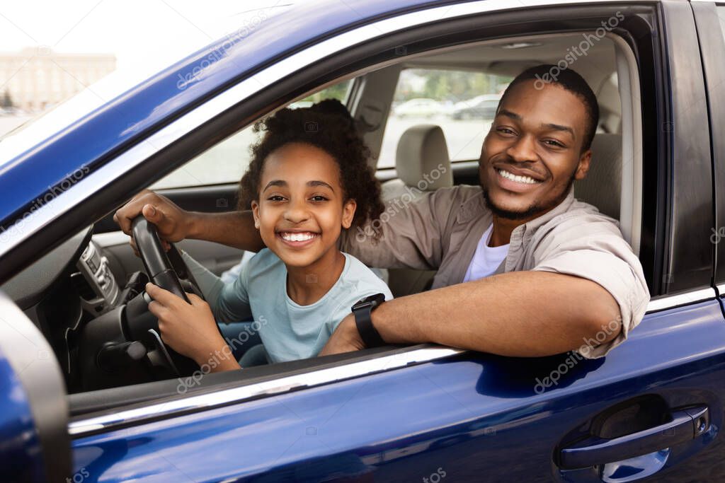 Happy Black Daddy Teaching Preteen Daughter To Drive Smiling To Camera, Sitting In Drivers Seat With Father Together. Child Learning To Drive Auto Having Fun Traveling By Automobile
