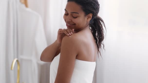 自己甘やかす概念 肩にボディクリームを塗るタオルに包まれた美しい黒の女性は 自宅でお風呂の後に保湿スキンローションを使用し 選択的な焦点 — ストック動画