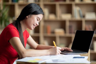 Neşeli ergenlik çağındaki Japon bayan ev ödevi yapıyor, oda içinde ders çalışan boş ekranlı dizüstü bilgisayarla sınava hazırlanıyor. Aygıt, eğitim ve iş, sosyal uzaklık ve evde yeni normallik, covid-19