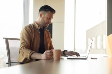 Ofiste çalışan bir iş adamının dizüstü bilgisayarlı daktilo kullanırken yan görüntüsü. İş yerinde interneti tarayan erkek. İçerideki masada oturuyor. Teknoloji ve İş Konsepti