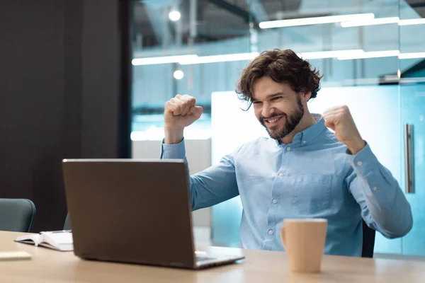 Excited mature businessman celebrating achievement, making great deal or agreement, gesturing YES near laptop at modern office, copy space. Achieving success, professional triumph concept