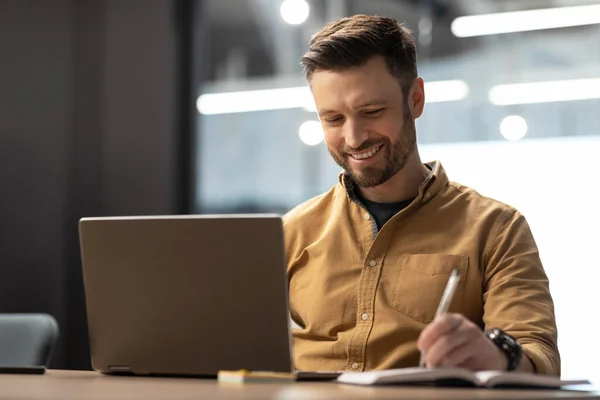 Cheerful Business Guy Using Laptop Working Online Taking Notes Writing — Foto de Stock